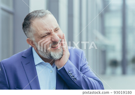 Close-up photo portrait of senior gray-haired businessman, experienced businessman outside office building, having severe toothache Close-up photo portrait of senior gray-haired businessman, experienced businessman outside office building, having severe toothache 93019180