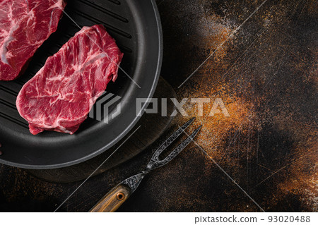 Uncooked Shoulder Top Blade or flat iron beef meat steaks, on old dark rustic table background, top view flat lay, with copy space for text 93020488