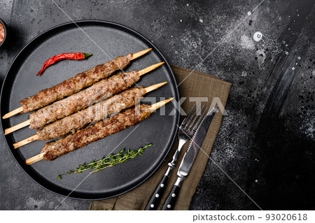 Kofta or lula beef and lamb meat kebabs skewers, on plate, on black dark stone table background, top view flat lay, with copy space for text Kofta or lula beef and lamb meat kebabs skewers, on plate, on black dark stone table background, top view flat lay, with copy space for text 93020618