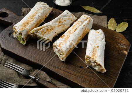 Eastern traditional shawarma with chicken and vegetables, on cutting board, on black wooden table background Eastern traditional shawarma with chicken and vegetables, on cutting board, on black wooden table background 93020751
