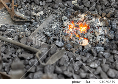 Close-up detail old medieval blacksmith furnace with hot burning coal flame forge iron metal. Craft smith farrier workshop fireplace with many professional craftsman tools equipment 93020819