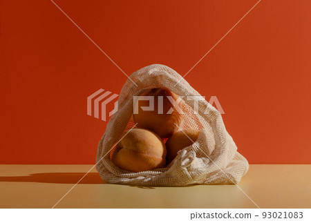 Peaches in a reusable cotton string bag on bright background 93021083