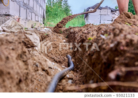 Construction worker is digging trench for laying cables, using shovel to excavate soil. Construction worker is digging trench for laying cables, using shovel to excavate soil. 93021133