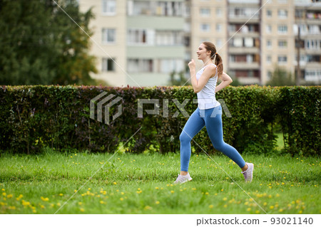 Young woman in leggings and tank top is doing morning run. 93021140