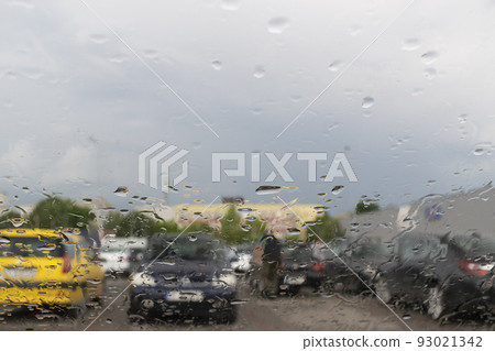 Raindrops on the window glass with outline of a car and a person Raindrops on the window glass with outline of a car and a person 93021342