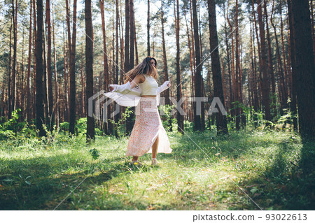 Young beautiful hippie woman walks in the summer forest laughs dances and enjoys life and nature Young beautiful hippie woman walks in the summer forest laughs dances and enjoys life and nature 93022613