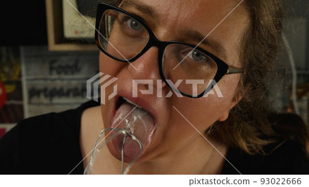 Close-up of the girl with glasses with her tongue licking the cream cheese cream from the whisk. The baker's concept. Cooking a cake in the home kitchen. 93022666