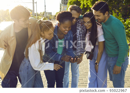 Multiracial young people bending over looking at screen of phone and smiled stand on city streets Multiracial young people bending over looking at screen of phone and smiled stand on city streets 93022967