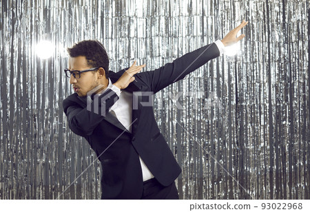 Happy confident black man in a tuxedo suit and glasses dancing and having fun at a party 93022968
