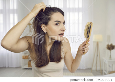 Woman who's worried by problem of hair loss or scalp dandruff is looking in mirror 93022995