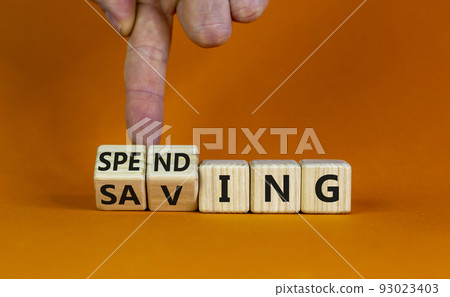 Saving or spending symbol. Businessman turns cubes and changes the word 'spending' to 'saving'. Beautiful orange table, orange background, copy space. Business and saving or spending concept. 93023403