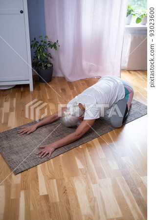 woman kneeling on a mat and doing a balasana asana while practicing yoga at home woman kneeling on a mat and doing a balasana asana while practicing yoga at home 93023600