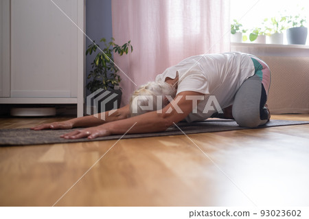 woman kneeling on a mat and doing a balasana asana while practicing yoga at home woman kneeling on a mat and doing a balasana asana while practicing yoga at home 93023602