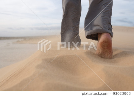 A man walks along the sandy beach. In the air, grains of sand fly from a strong wind. A man walks along the sandy beach. In the air, grains of sand fly from a strong wind. 93023903