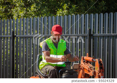 A man on a mini-excavator levels a piece of land, loosens the soil. A man on a mini-excavator levels a piece of land, loosens the soil. 93024329