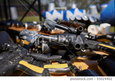 Close up of paintball gun, special balls and protective mask, equipment for playing paintball on a wooden table, action game concept. Close up of paintball gun, special balls and protective mask, equipment for playing paintball on a wooden table, action game concept. 93024402
