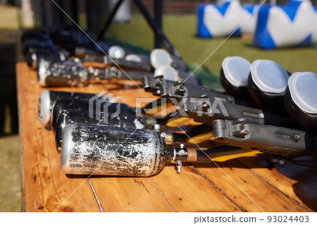 Close up of paintball gun, special balls and protective mask, equipment for playing paintball on a wooden table, action game concept. Close up of paintball gun, special balls and protective mask, equipment for playing paintball on a wooden table, action game concept. 93024403