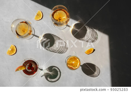 Summer cocktails with fruit in the sunlight. Fresh juicy beverages in glasses with shadows making trendy pattern on beige background. Delicious lemonade, cold tea, soda and water  93025283