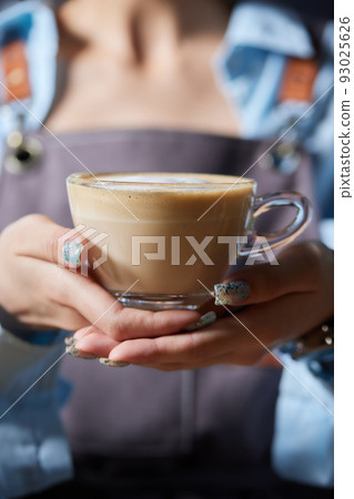 Top view shot of professional barista pouring milk from jar in to a cup of coffee, coffee being prepared by a barista. Focus on hands holding cup of coffee. Top view shot of professional barista pouring milk from jar in to a cup of coffee, coffee being prepared by a barista. Focus on hands holding cup of coffee. 93025626