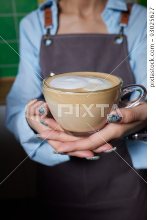 Top view shot of professional barista pouring milk from jar in to a cup of coffee, coffee being prepared by a barista. Focus on hands holding cup of coffee. 93025627
