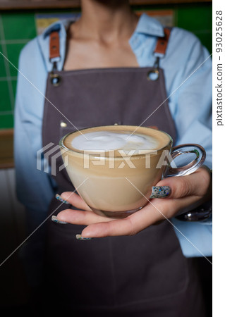 Top view shot of professional barista pouring milk from jar in to a cup of coffee, coffee being prepared by a barista. Focus on hands holding cup of coffee. Top view shot of professional barista pouring milk from jar in to a cup of coffee, coffee being prepared by a barista. Focus on hands holding cup of coffee. 93025628