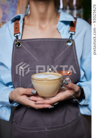 Top view shot of professional barista pouring milk from jar in to a cup of coffee, coffee being prepared by a barista. Focus on hands holding cup of coffee. 93025629