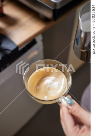 Top view shot of professional barista pouring milk from jar in to a cup of coffee, coffee being prepared by a barista. Focus on hands holding cup of coffee. 93025634