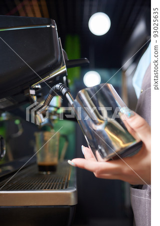 Top view shot of professional barista pouring milk from jar in to a cup of coffee, coffee being prepared by a barista. Focus on hands holding cup of coffee. Top view shot of professional barista pouring milk from jar in to a cup of coffee, coffee being prepared by a barista. Focus on hands holding cup of coffee. 93025635