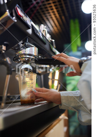 Top view shot of professional barista pouring milk from jar in to a cup of coffee, coffee being prepared by a barista. Focus on hands holding cup of coffee. 93025636