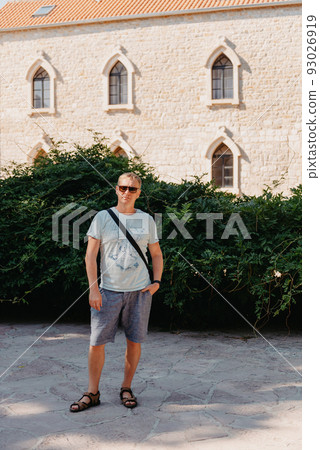 A handsome young man standing and smiling happily in the background of urban buildings. Forty years old caucasian tourist man outdoor near old city buildings - summer holiday. A handsome young man standing and smiling happily in the background of urban buildings. Forty years old caucasian tourist man outdoor near old city buildings - summer holiday. 93026919