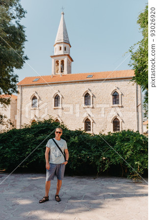 A handsome young man standing and smiling happily in the background of urban buildings. Forty years old caucasian tourist man outdoor near old city buildings - summer holiday. 93026920