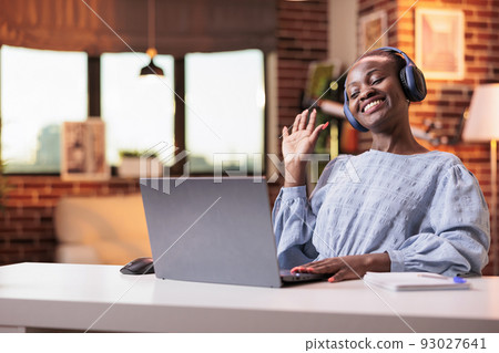 African american female employee greeting coworkers on videocall while sitting in modern home office. Videoconference meeting with company remote team, businesswoman on teleconference African american female employee greeting coworkers on videocall while sitting in modern home office. Videoconference meeting with company remote team, businesswoman on teleconference 93027641