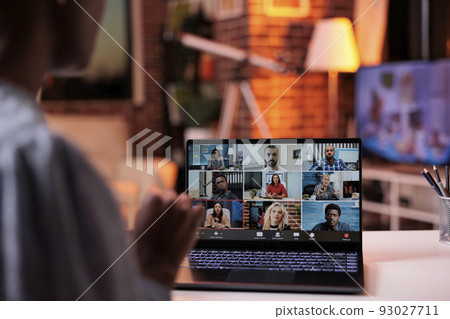 Company employee brainstorming with coworkers on online business meeting. African american female corporate worker chatting with colleagues on videocall using laptop in office with warm sunset light 93027711