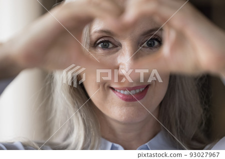 Happy lady looking at camera through hand heart at eyes 93027967
