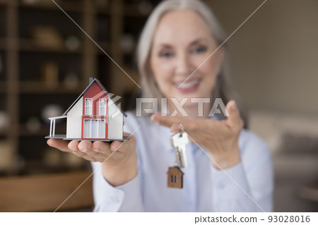 Happy mature mortgage broker woman holding keys and small model 93028016