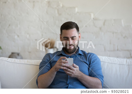 Cheerful customer man using mobile phone at home Cheerful customer man using mobile phone at home 93028021