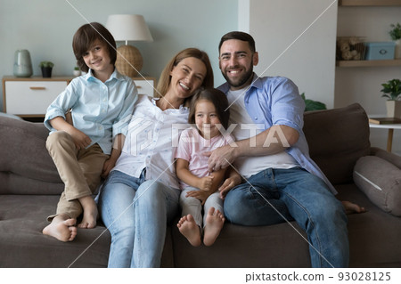 Happy couple with children posing for camera seated on couch Happy couple with children posing for camera seated on couch 93028125