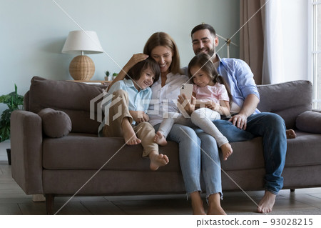 Couple with little children sit on couch using cellphone Couple with little children sit on couch using cellphone 93028215