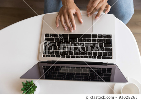 Young woman using laptop, sitting at coffee table, typing 93028263
