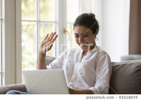 Cheerful positive Indian laptop user woman waving hand hello Cheerful positive Indian laptop user woman waving hand hello 93028659