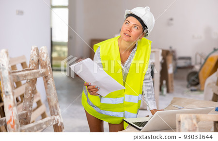 Portrait of a young woman with documents, checking the house repair plan on a laptop Portrait of a young woman with documents, checking the house repair plan on a laptop 93031644