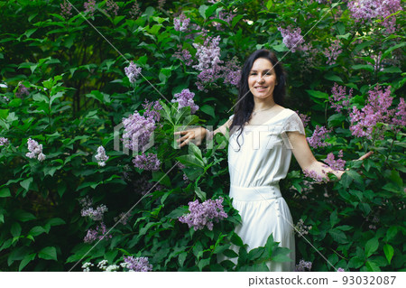 Portrait of an attractive woman surrounded by lilac bushes. Spring and summer, seasonal photos. Front view. 93032087