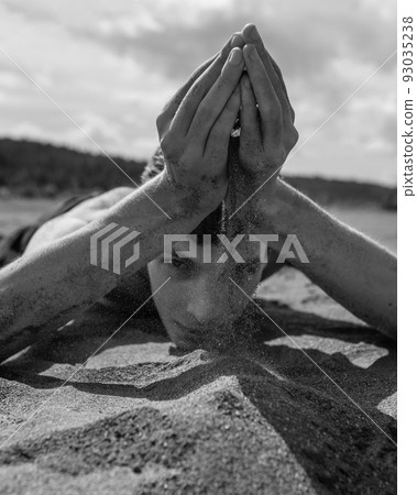 Man lying on his stomach and pouring sand through hands in the desert Man lying on his stomach and pouring sand through hands in the desert 93035238