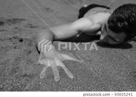 Man lying on his stomach on sand in desert. Selective focus on hand in foreground 93035241