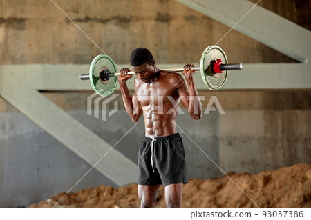 Athletic black young man lifting a heavy-weight barbell in outdoor gym under the bridge. Healthy lifestyle concept Athletic black young man lifting a heavy-weight barbell in outdoor gym under the bridge. Healthy lifestyle concept 93037386