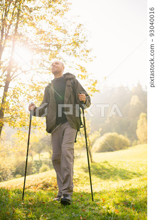 View from below of a young male traveler with trekking sticks in his hands standing in the sun. 93040016