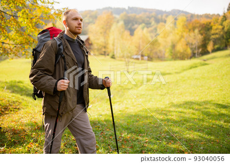 Male adventurer hiking in the mountains with a backpack and trekking sticks in his hands. 93040056