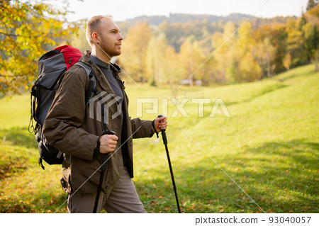 View of a profile of a male hiker traveling in the mountains with a backpack and trekking sticks. View of a profile of a male hiker traveling in the mountains with a backpack and trekking sticks. 93040057