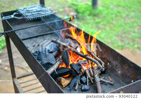 an empty brazier with a burning bonfire fire against the background of green grass preparing for a barbecue. 93040122
