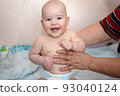naked caucasian boy in a diaper sits and laughs with two milk bottom teeth, his grandmothers hands hold him. 93040124
